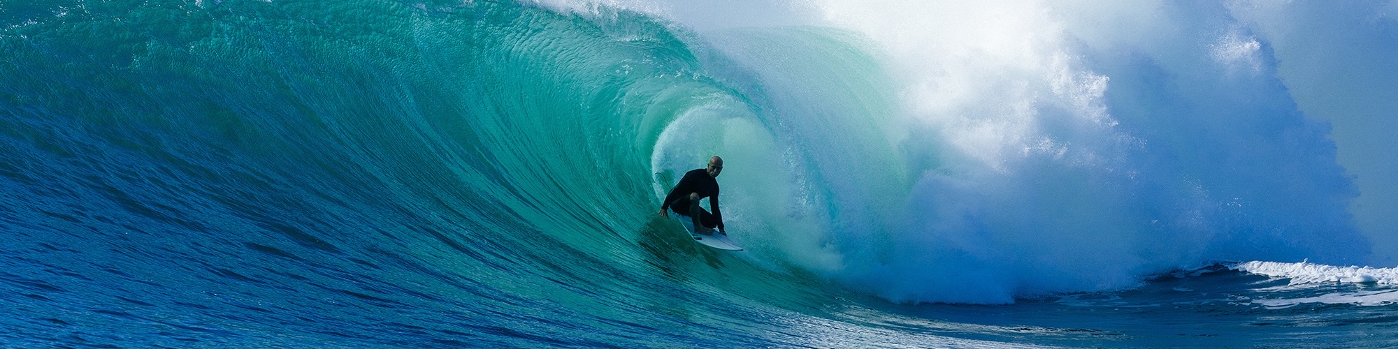 A surfer sits deep in an emerald barrel as a mate throws a shaka